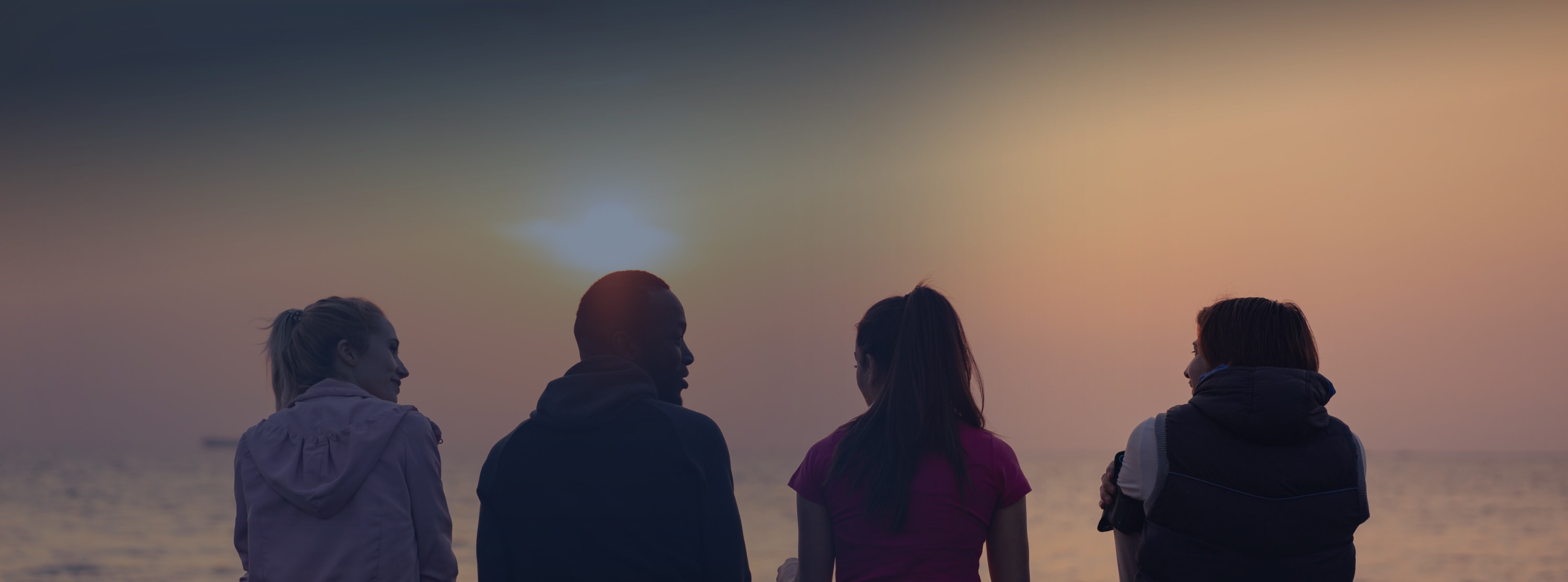 Four people are sitting in front of a sunset.