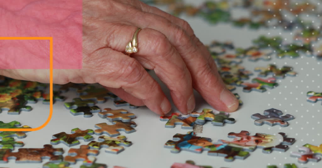 An elderly hand moving jigsaw puzzle pieces