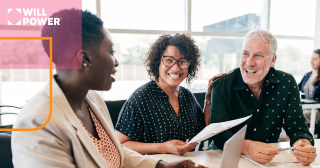 Group of adults in a business setting, sitting around a table and smiling.
