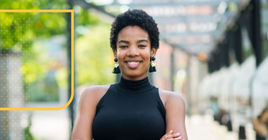 A woman with short curly hair is standing, smiling, with her arms crossed.