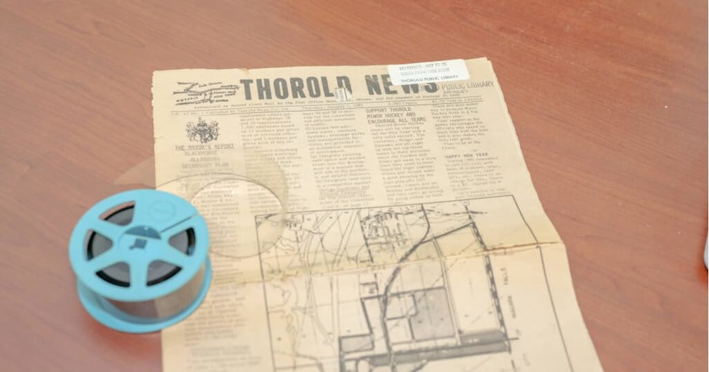 A microform reel alongside a physical copy of the Thorold News newspaper.