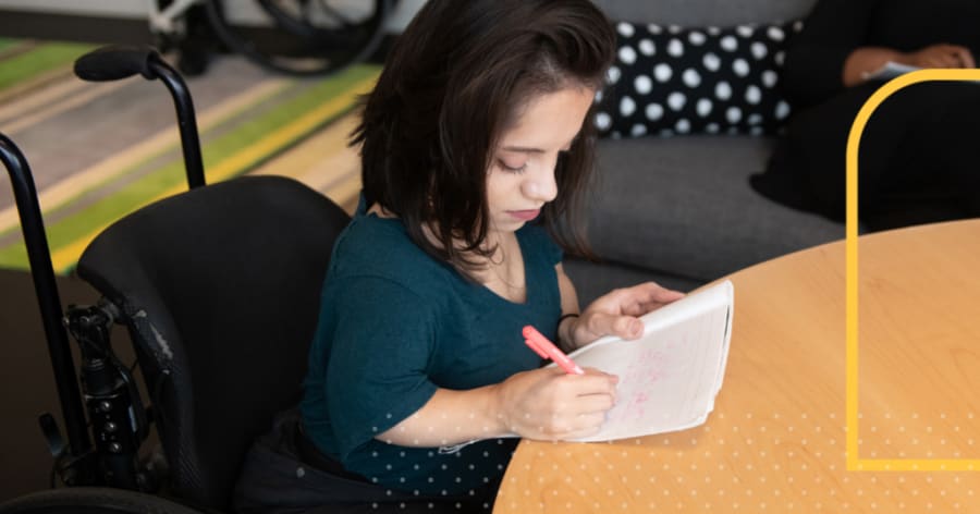A woman in a wheelchair is writing on some paper.