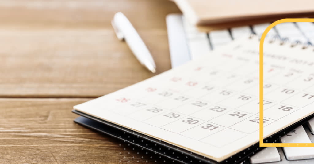 Pen and paper calendar on a wooden desk.