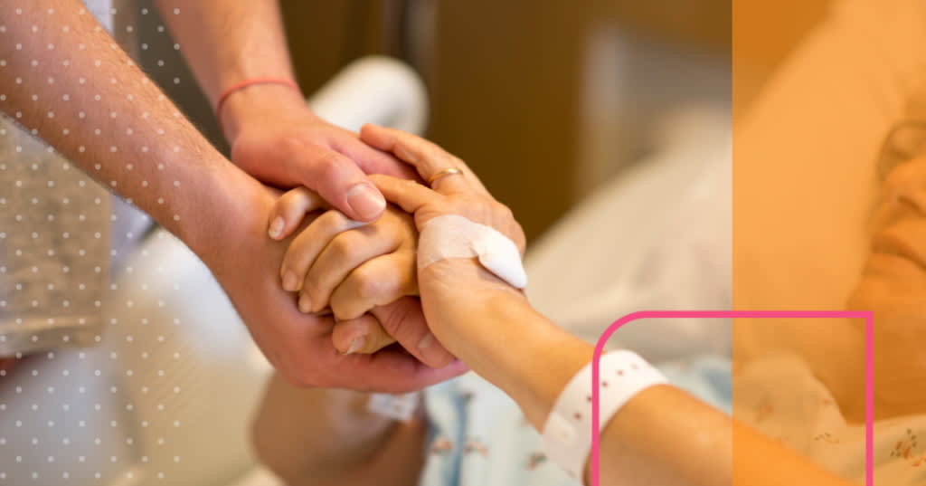 Closeup of younger hands lovingly holding the hands of an older person in hospital.