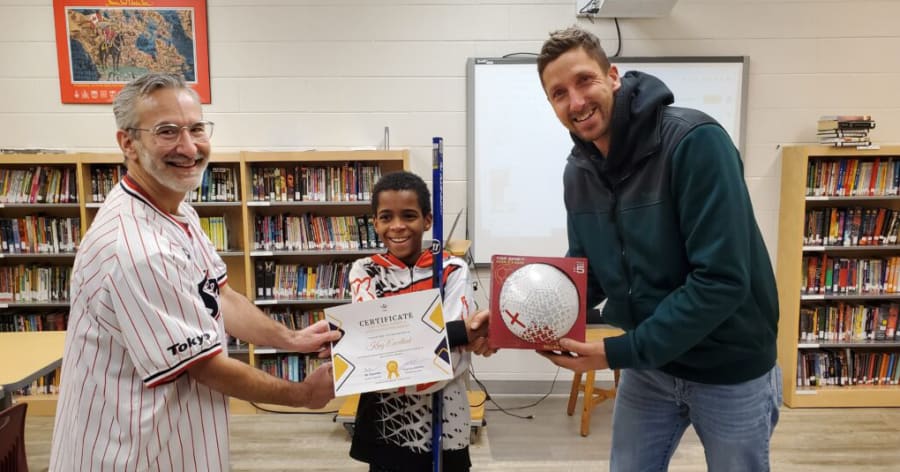 Two men present a young boy with a ball and a certificate.