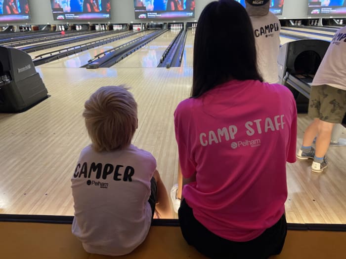 A child from a Pelham summer camp sits with a camp staff member at a bowling alley.