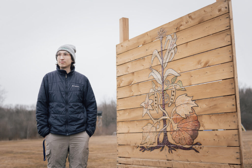 Adam Pounds, co-founder of Simple Abundance Farm, standing next to a wooden art installation that pays tribute to the "Three Sisters"