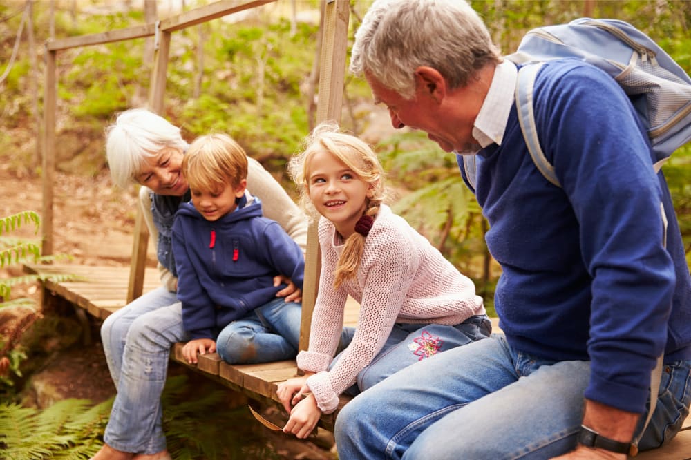 Two young kids are sitting on a wooden bridge with their grandparents.